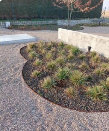 Bordura metálica curva delimitando un macizo de grava y plantas