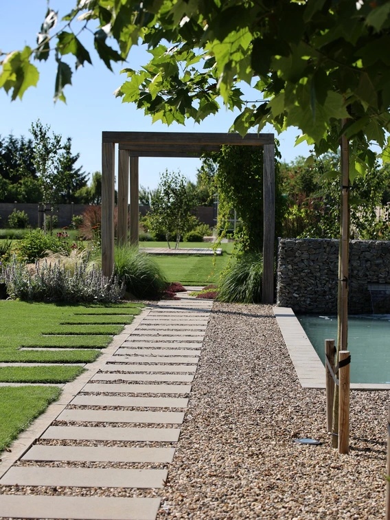 Jardín con piscina y camino de grava junto a fachada blanca en verano